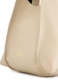 Beżowa skórzana torebka o zaokrąglonym kształcie, charakteryzująca się gładką fakturą. Nazwa marki "VENEZIA" wytłoczona na złoto z przodu.