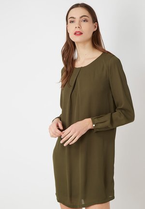 Vestido verde oliva con mangas largas, detalle de pliegues en la parte delantera, escote redondo y botones decorativos en los puños. Tela suave y ligera.