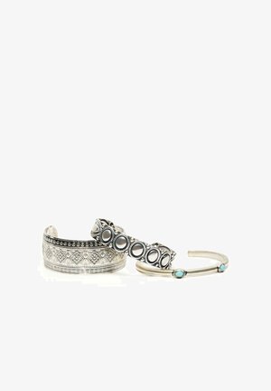 Trois bracelets manchettes en argent ; un avec des motifs géométriques, un avec des découpes circulaires, et un fin avec deux petites pierres turquoise.