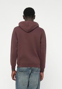 Pulloverkort i mørk mahogni; lavet af blød bomuld, har en snoretrækshætte og ribbede manchetter, parret med lyseblå denimjeans.