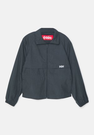 Mustmust sweater musta kõrge kraega, millel on kaks esimest taskut, elastsed mansetid ja kollases sildis krae sees.