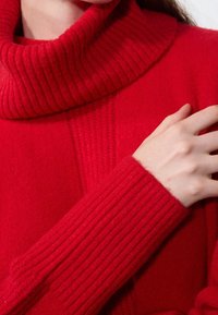 Czerwony sweter z golfem o prążkowanej fakturze i mankietach. Posiada pionowe wykończenie dzianiny z przodu. Miękka tkanina, dopasowany krój.
