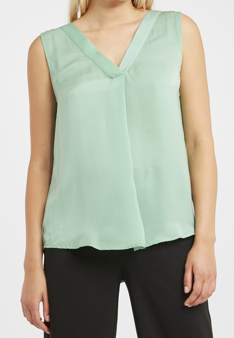Blusa sin mangas de color verde claro con escote en forma de V y diseño fluido. Fabricada con una tela suave que tiene un brillo sutil.