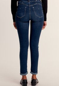 Blauwe skinny jeans van denim, met een hoge taille, opgerolde boorden en minimalistische details op de achterzakken. Fluweelachtige textuur overal.