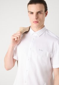 Polo shirt bianco a maniche corte con colletto a bottoni, caratterizzato da un discreto logo "BOSS" in rilievo sul lato sinistro del petto e una texture di tessuto liscia.