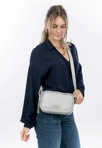 Borsa a tracolla grigia in pelle con bordi intrecciati, forma rettangolare, tracolla regolabile e piccolo logo metallico sul davanti.