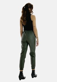 Grüne Jogginghosen aus Kunstleder mit elastischem Bund und Bündchen, kombiniert mit einem engen schwarzen Tanktop. Glatte Textur und taillierter Schnitt.