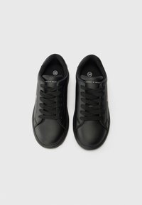 Baskets noires en matériau synthétique lisse, avec un design classique à lacets, une doublure texturée et un petit logo sur la languette.