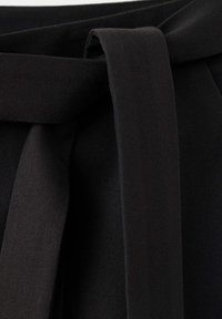 Gros plan d'une ceinture en tissu noir nouée en un nœud simple sur un vêtement noir assorti.