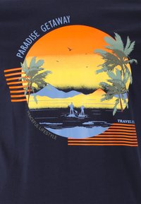 Marinblå t-shirt med en solnedgångsgrafik som innehåller palmträd, berg och paddelbrädåkare, accentuerad av orange och ljusblå linjer och text.