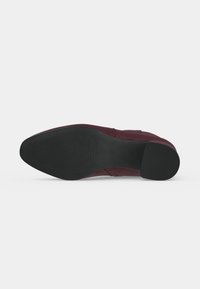 Semelle noire d'une chaussure en cuir bordeaux vue par le dessous, présentant un talon lisse et une semelle avant texturée pour l'adhérence sur fond blanc.