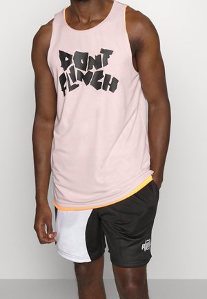 Homme portant un t-shirt sans manches rose avec le texte "NE REAGIS PAS" et un short noir et blanc avec le logo Puma sur une jambe.