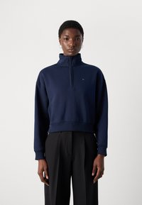 Navy blue zip-up sweatshirt with a high collar, ribbed cuffs, and hem. Small logo accent on the left chest, relaxed fit design.