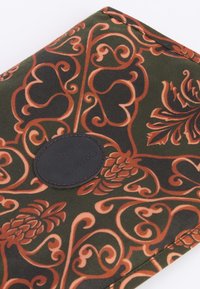 Τσαντάκι με σχέδιο από ύφασμα σε σκούρο πράσινο με πορτοκαλί σπείρες και λουλουδάτα μοτίβα; διαθέτει στρογγυλή δερμάτινη ταμπέλα λογότυπου καφέ.