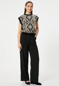 Suéter de punto con un patrón geométrico en negro y crema, de mangas cortas y un dobladillo ajustado. Combinado con pantalones de pierna ancha de tiro alto en negro.