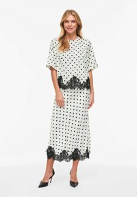 Ensemble robe deux pièces à pois en crème et noir. Comprend un haut à coupe ample avec manches courtes et un ourlet orné de dentelle sur les deux pièces.