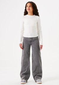 Witte langekousen geribbelde shirt gecombineerd met grijze wijde jeans. De jeans hebben een klassieke wasbeurt en een rechte snit tot aan de enkels.