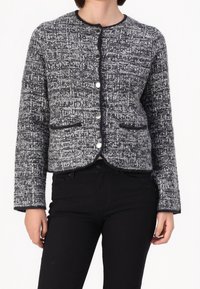 Giacca nera e bianca dalla texture particolare con scollo rotondo, chiusura frontale con bottoni e due tasche frontali. Le maniche sono leggermente svasate.