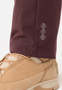 Maroon broek met een gladde textuur, voorzien van een zijnaad die wordt benadrukt door drie embroidereerd diamantenvormige details, gecombineerd met beige schoeisel.