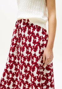 Witte bloemenrok met een levendig rood bloemmotief, zacht materiaal en een geplooid ontwerp. De tailleband zit comfortabel op de taille.