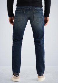 Temno modri kavbojke s ravnim krojem, pet žepov, svetlimi odtenki obarvanosti in zakrivljenim hrbtnim delom, v kombinaciji s bež supergami z črnimi detajli.