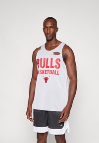Jersey de baloncesto de malla blanca con el texto y logo en rojo "BULLS BASKETBALL". Se lleva con pantalones cortos de malla negra y un ribete blanco en el dobladillo.