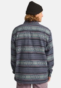 Chemise en flanelle à motifs pour hommes dans des tons de bleu foncé et de vert, avec des rayures horizontales et des accents texturés, offrant une coupe décontractée.