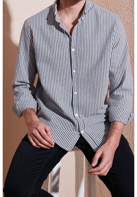 Knoop-up shirt met marineblauwe en witte strepen, lange mouwen en een mandarinokraag. De stof lijkt textuur te hebben met een ontspannen pasvorm.