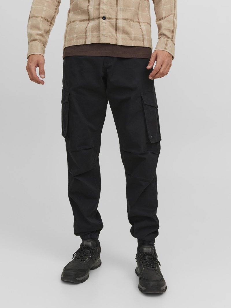 Black cargo pants with multiple side pockets, tapered cuffs, and a smooth fabric texture, paired with dark athletic shoes.