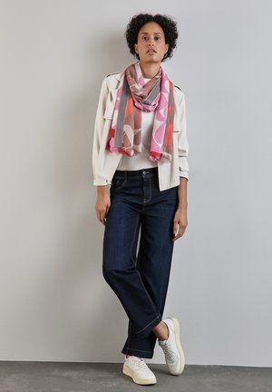 Cotton scarf in pink and brown geometric patterns, worn over a white top and light jacket. Dark blue wide-leg jeans and white sneakers.