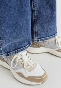Sko med hvit, beige og grå fargekombinasjon; glatt skinn og semsket skinn; har snøring og en strukturert såle; kombinert med blå denim.