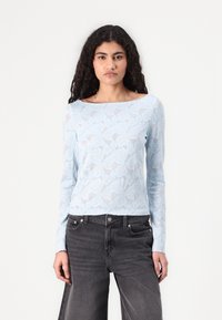Light blue long-sleeve top with floral lace design, sheer texture, wide neckline, paired with dark gray high-waisted jeans.