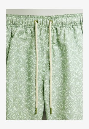 Jasnozielone szorty w wzory z elastycznym paskiem. Wzór składa się z białych kropek w diamentowym i kwiatowym wzorze.