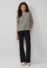 Gestreifte silberne Bluse mit weitem Ausschnitt und kurzen Ärmeln, kombiniert mit schwarzen Schlaghosen und weißen Riemchensandalen. Glatte Textur.