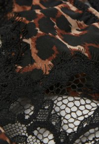 Leopardpræget stof i nuancer af brunt og sort, med detaljeret sort blondekant med et hexagonalt mønster og bølgede kanter.