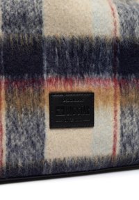 Tkanina w kratę wełnianą w kolorze granatowym, kremowym i rdzawym; posiada czarną skórzaną metkę z napisem "BIG STAR" i tekstem. Miękka, teksturowana powierzchnia.