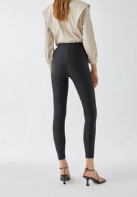 Hooggetailleerde zwarte leggings met een gladde, rekbare textuur, gecombineerd met een lichtbeige top met pofmouwen en een rechte achterkant.