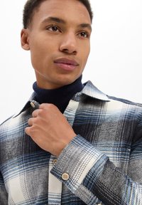 Geruite shirt in tinten van blauw, zwart en wit; heeft een knoopsluiting aan de voorkant, een puntige kraag en een textuurstof met contrasterende manchetten.