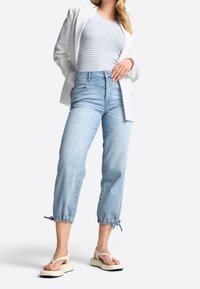 Jeans cortos azul claro con tobillos fruncidos; combinados con una blusa de rayas azul claro y blanco y un blazer blanco texturizado. Sandalias gruesas color crema.