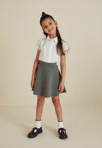 Witte kortekraag overhemd met knopen, gecombineerd met een grijze uitlopende rok. Zwarte schoenen met witte accenten en witte sokken maken de look compleet.