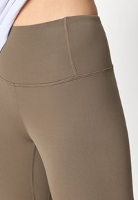 Aukštai taliai leggingai muted rudo atspalvio. Pagaminti iš elastingos medžiagos su lygiomis siūlėmis ir glotnia tekstūra. Ypatinasi minimalistišku dizainu.