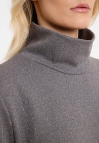Grauer Rollkragenpullover aus weichem Material, mit vertikalen Streifen aus kontrastierendem metallischem Goldfaden und einem hohen Kragen. 