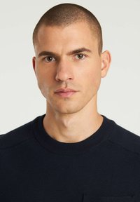 Maglione lavorato a maglia blu navy con scollo rotondo, caratterizzato da un tessuto testurizzato e un piccolo dettaglio tasca sul lato sinistro del petto.