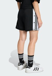 Čierne športové šortky s bielymi bočnými panelmi s tromi prúžkami a cvokmi. Nosené s čierno-bielymi pruhovanými ponožkami a bielymi teniskami.