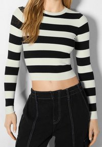 Haut court à manches longues rayé noir et crème avec une texture côtelée, un col rond, et une coupe ajustée, associé à un pantalon noir taille haute.