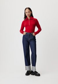 Pullover rosso lavorato a maglia con colletto a zip, abbinato a jeans in denim scuro a vita alta con orli sfilacciati e scarpe con plateau nere.