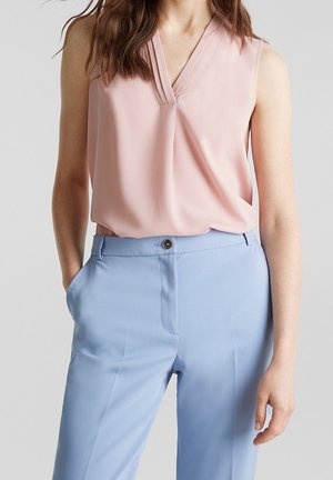 Różowa, bezrękawna bluzka z dekoltem w serek, zestawiona z jasnoniebieskimi, wysokim stanem spodniami z przodu zapinanymi na guziki i posiadającymi kieszenie.