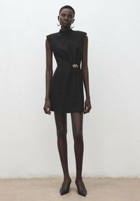 Černé mini šaty s vysokým límcem, strukturovanými rameny a zlatým akcentem v pase. Hladká tkanina a přiléhavý střih.