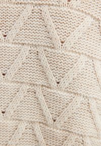 Beige gebreide stof met een textuurpatroon van afwisselende driehoeken en driehoeken met kleine openingen, die een zachte en dikke garen laat zien.