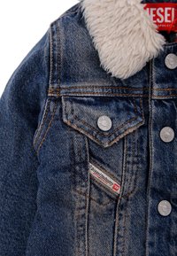 Veste en denim avec un col moelleux de couleur crème, dotée de boutons métalliques, de coutures orange, d'une poche poitrine et d'une étiquette de marque.
